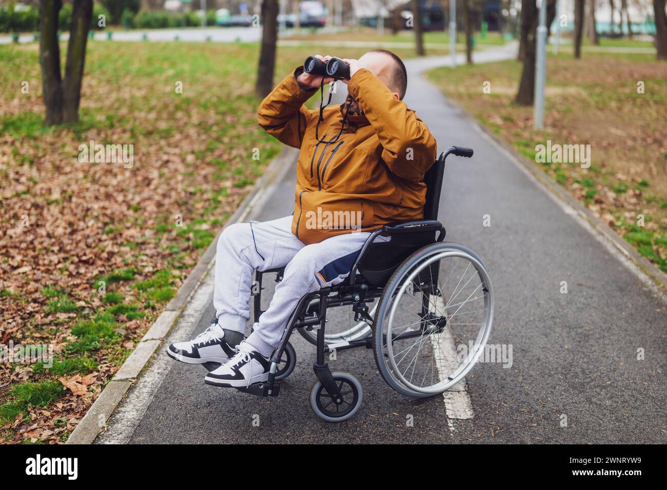 Un portatore di handicap paraplegico in sedia a rotelle utilizza un binocolo all'aperto. Sta osservando gli uccelli. Foto Stock