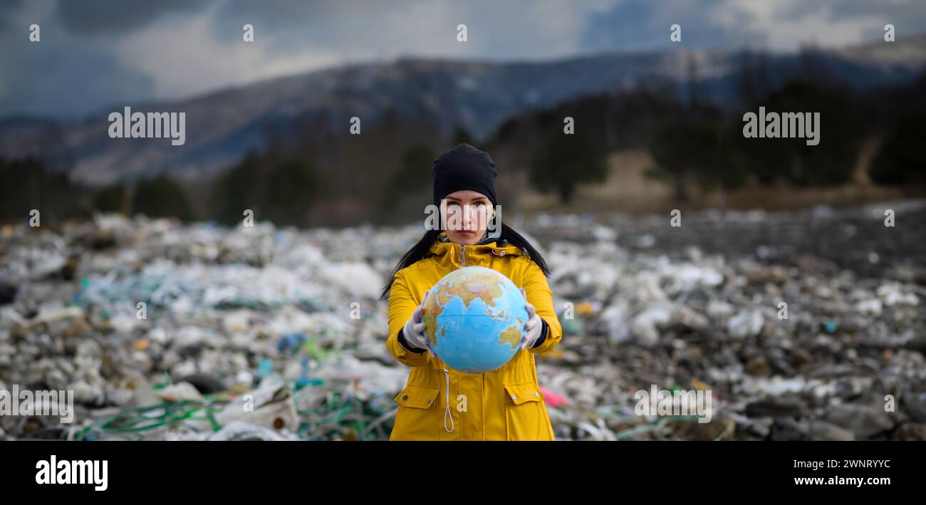 Attivista che tiene in mano il modello Eart, il globo, in discarica, una grande pila di rifiuti sulle coste marine, un concetto ambientale e un attivismo ecologico. Foto Stock