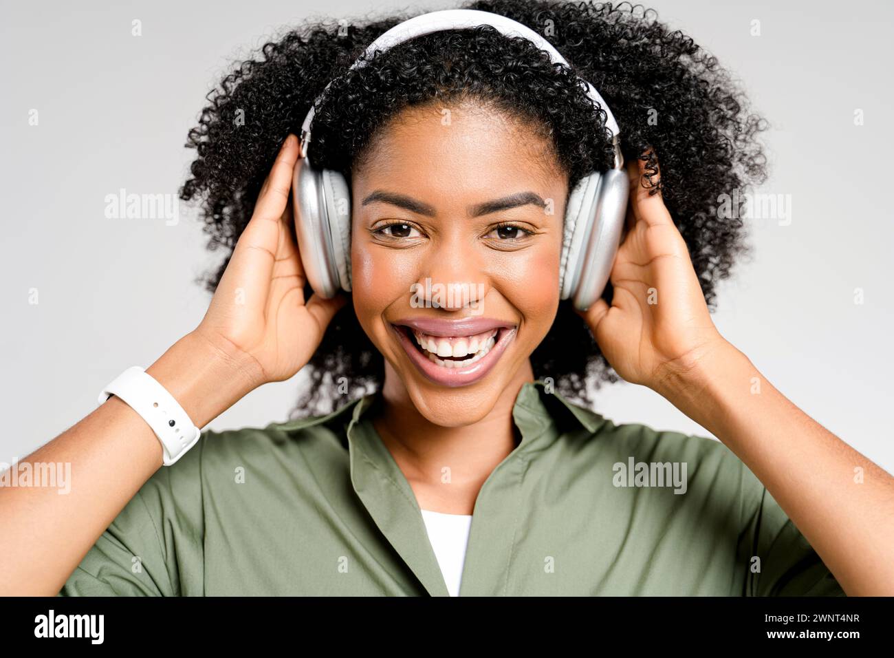 Una allegra donna afro-americana ama la musica preferita con le cuffie color argento, il suo sorriso trasuda la gioia della melodia. Lo studio-shot cattura l'essenza del tempo libero moderno e dell'intrattenimento digitale Foto Stock