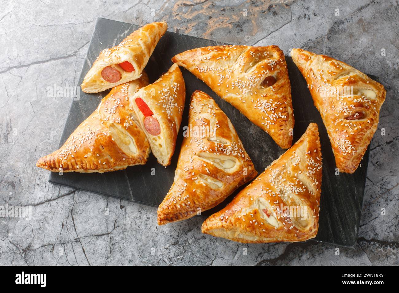 Maiali di pasta sfoglia in una coperta torte con salsiccia, formaggio, sesamo e pepe primo piano su un bordo di marmo sul tavolo. Vista dall'alto orizzontale Foto Stock