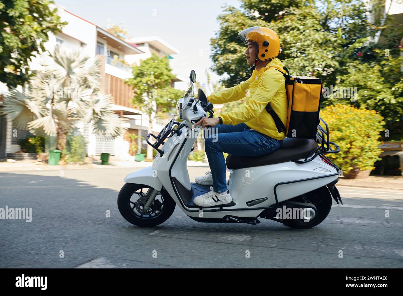 Vista laterale del giovane che lavora come corriere in moto Foto Stock