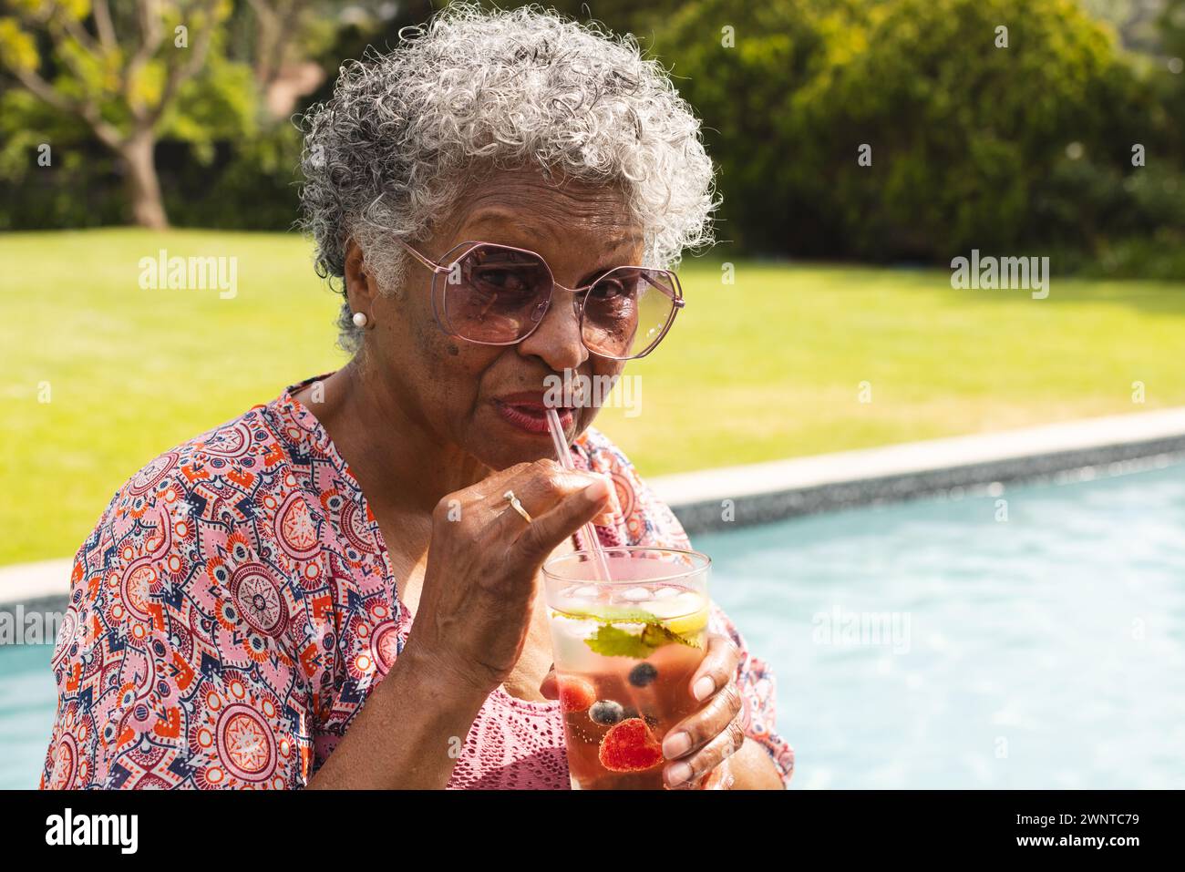 Una donna birazziale anziana sorseggia un drink in piscina Foto Stock