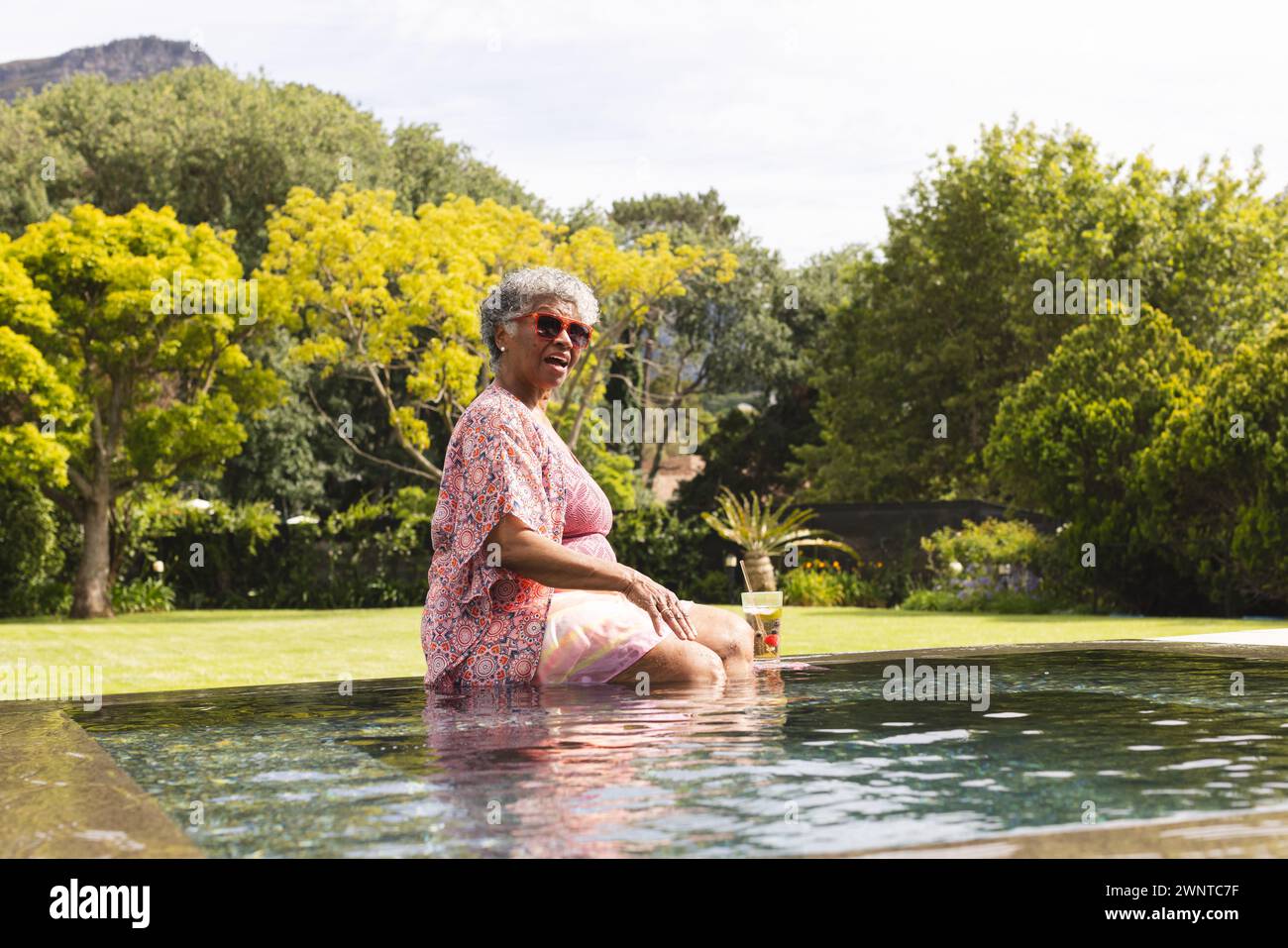 La donna birazziale senior gode di un momento a bordo piscina, mentre i suoi capelli grigi si abbinano alla giornata di sole Foto Stock