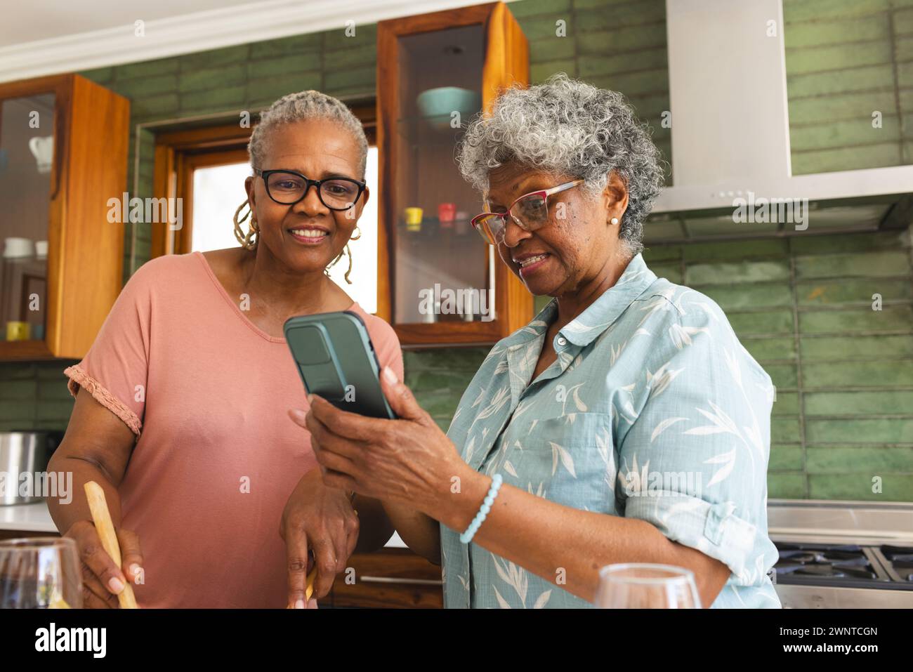 La donna afroamericana anziana e la donna birazziale senior condividono un momento in una cucina Foto Stock
