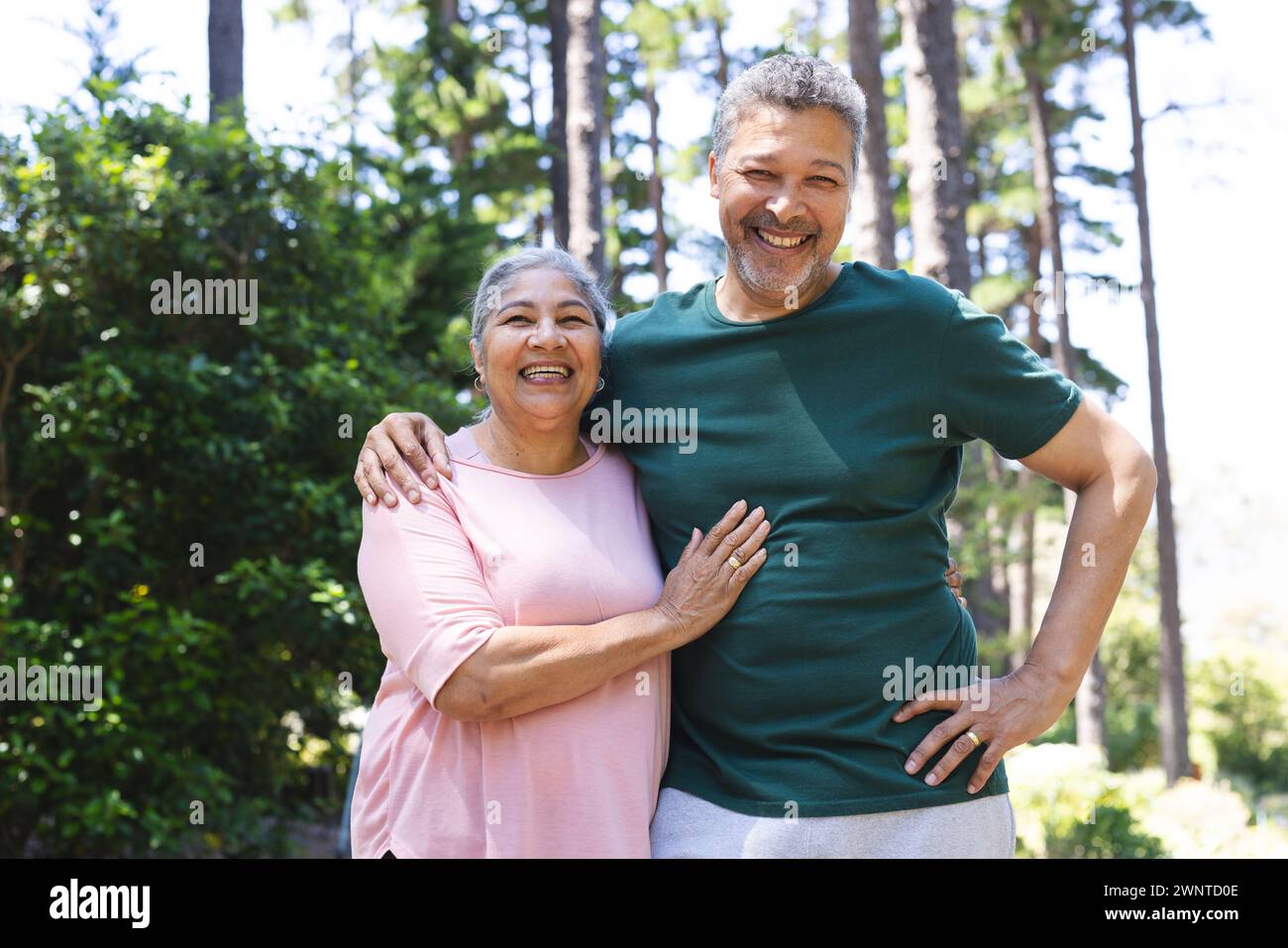 La coppia birazziale senior sorride calorosamente, in piedi all'aperto con alberi sullo sfondo Foto Stock