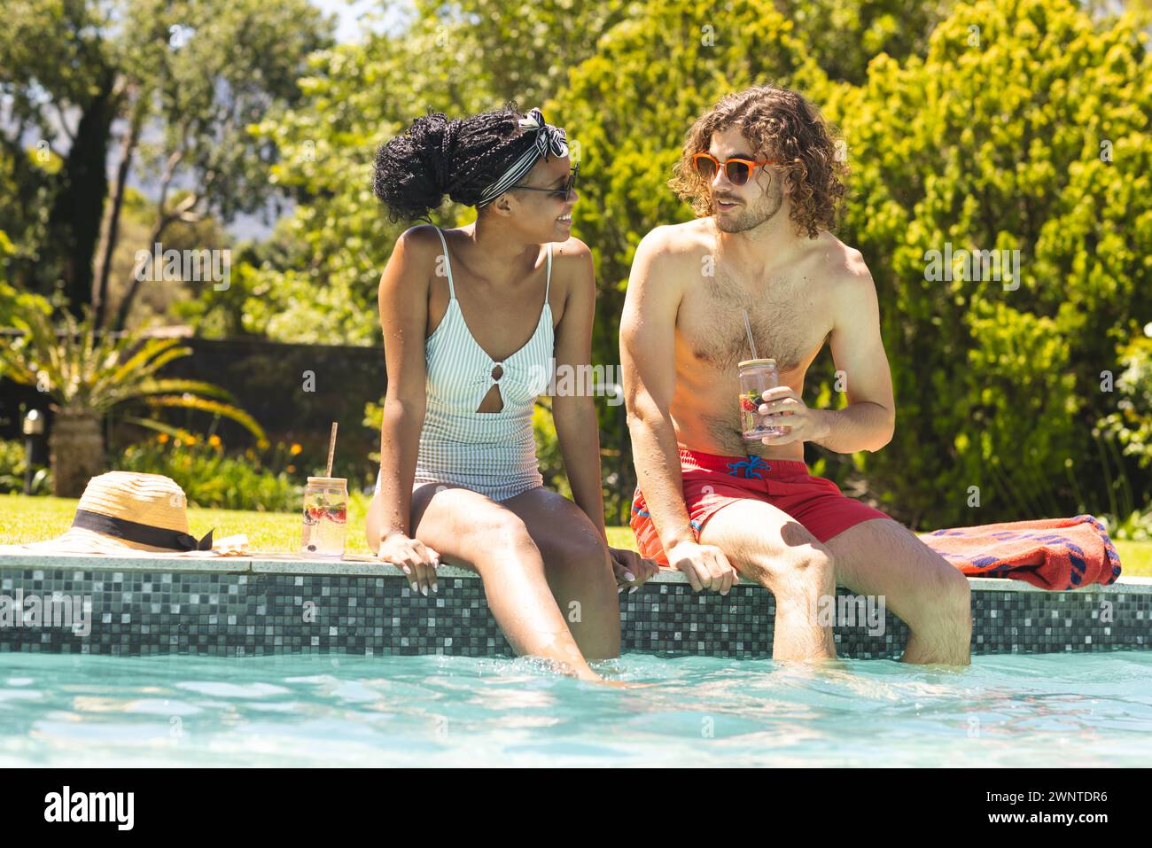 Coppia diversificata: Giovane donna afroamericana e giovane uomo caucasico si godono una giornata di sole a bordo piscina Foto Stock