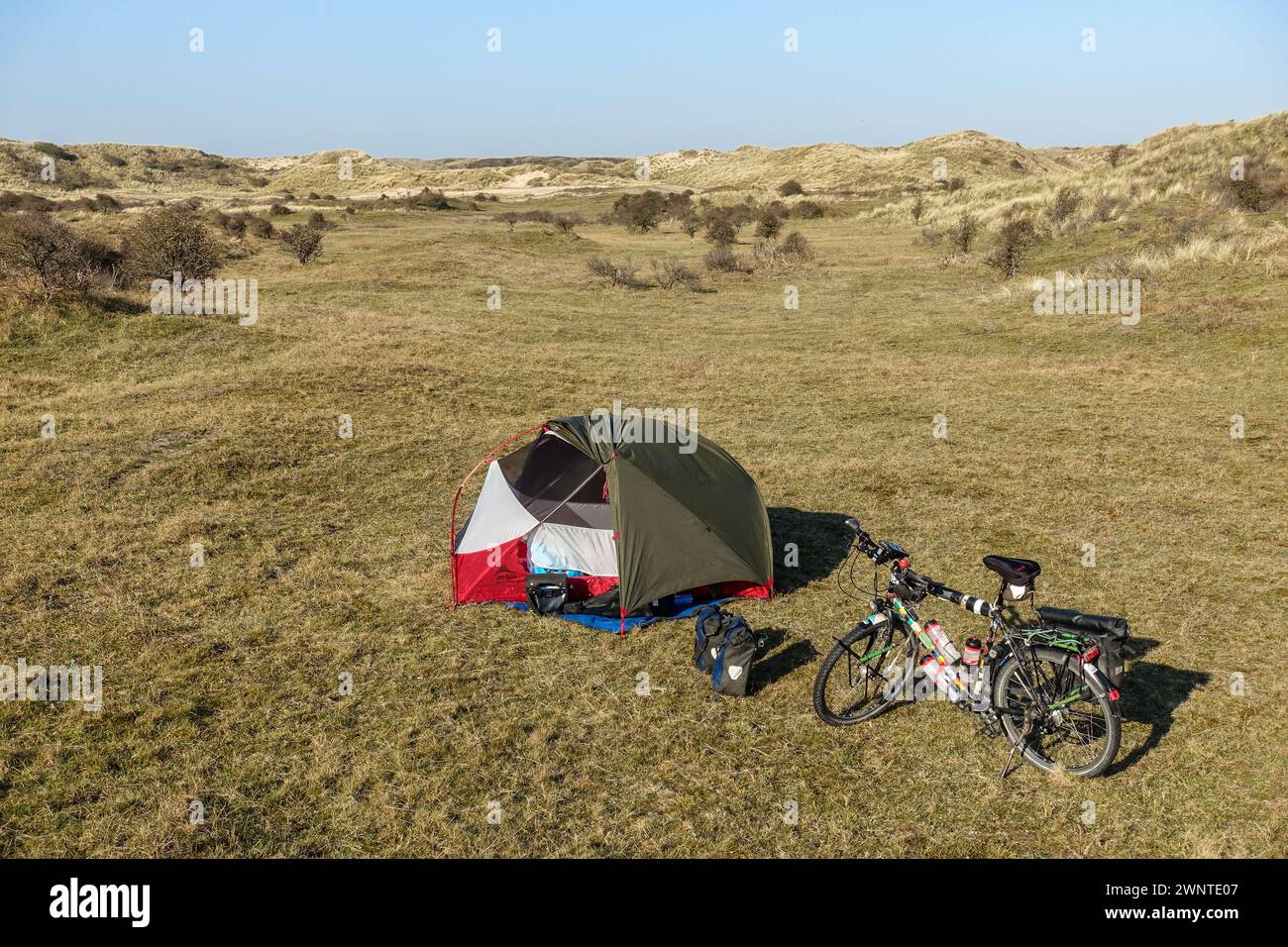 Tenda da campeggio e bicicletta in dune erbose sotto il cielo limpido, nell'Olanda settentrionale, Paesi Bassi Foto Stock