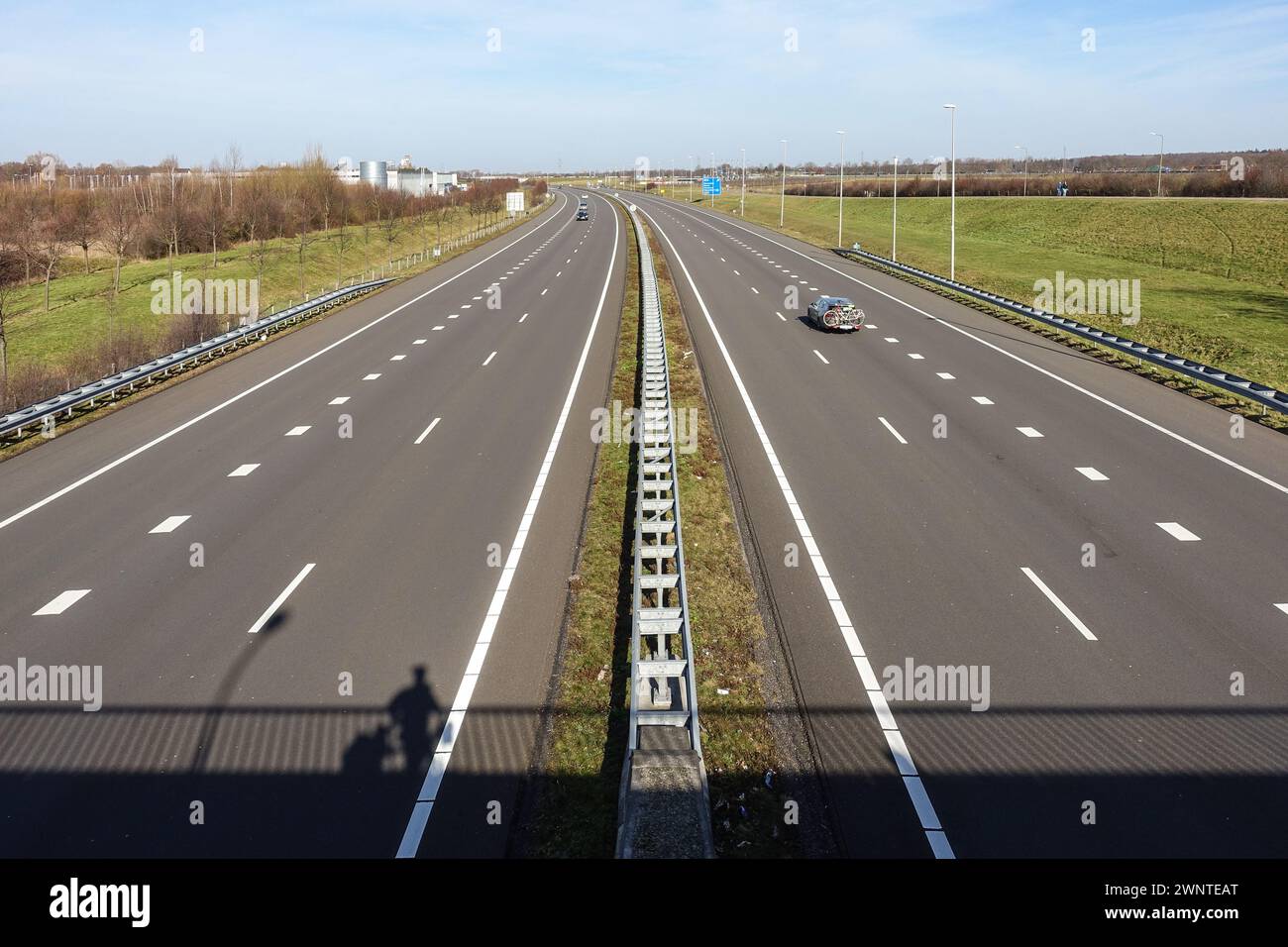 Autostrada a più corsie vuota con traffico e striscia verde mediana nel Limburgo, nei Paesi Bassi, con l'ombra di un uomo in piedi su un ponte sopra Foto Stock