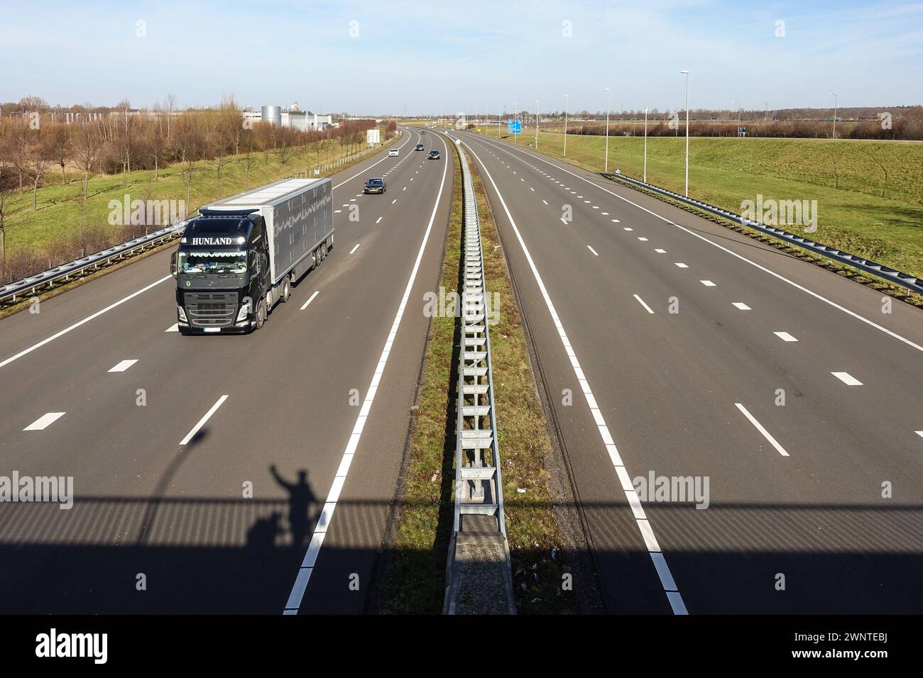 Autostrada a più corsie con traffico e striscia verde mediana nel Limburgo, nei Paesi Bassi, con l'ombra di un uomo in piedi su un ponte sopra Foto Stock