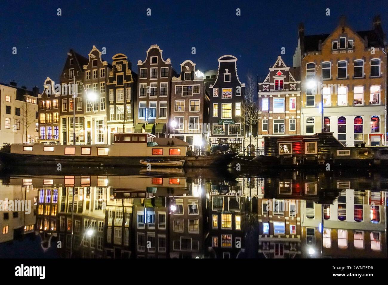Storici edifici olandesi illuminati di notte lungo un canale tranquillo di Amsterdam, che si riflettono sulla superficie dell'acqua. Foto Stock