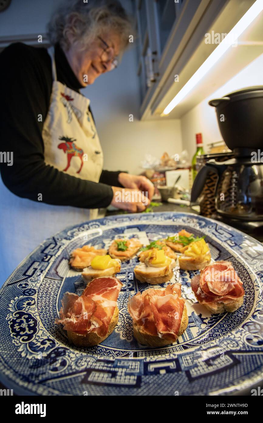 una donna prepara panini con specialità gastronomiche aperte su un grande vassoio di salice a casa Foto Stock