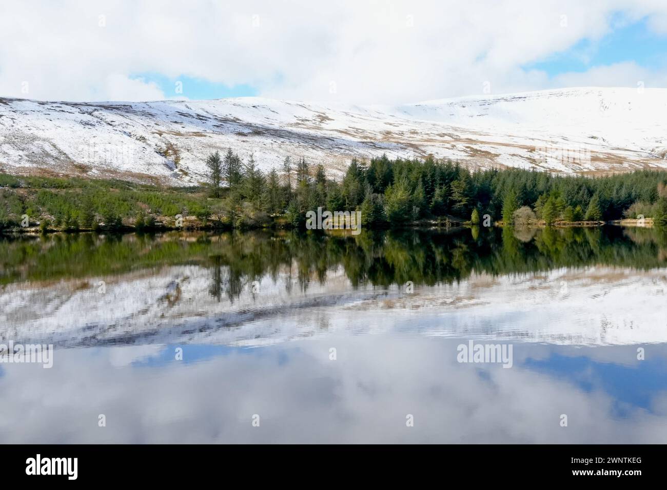 Paesaggio invernale e riflessi nell'acqua del bacino idrico gallese di Llwyn Onn, nel Brecon Beacons National Park. Montagne innevate ghiacciate Foto Stock