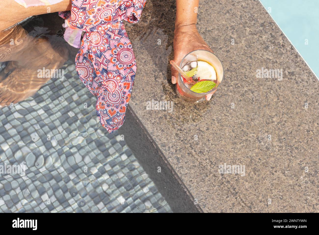 Una donna birazziale anziana gode di un rifugio a bordo piscina con spazio per le copie, mentre la sua mano regge un drink rinfrescante Foto Stock