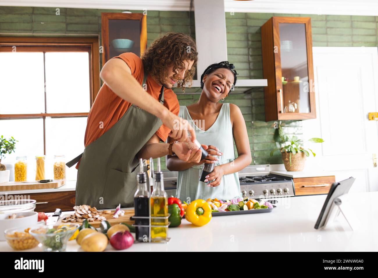 Coppia variegata, giovane donna afroamericana e uomo caucasico ridono mentre cucinano insieme Foto Stock