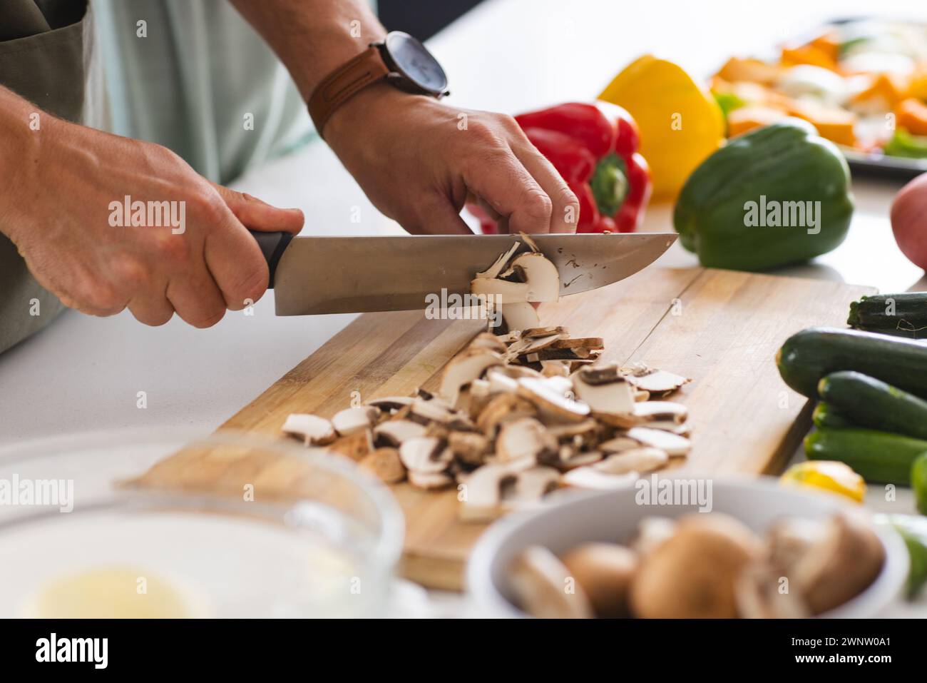 Una persona taglia i funghi su un tagliere bianco, circondato da peperoni colorati Foto Stock