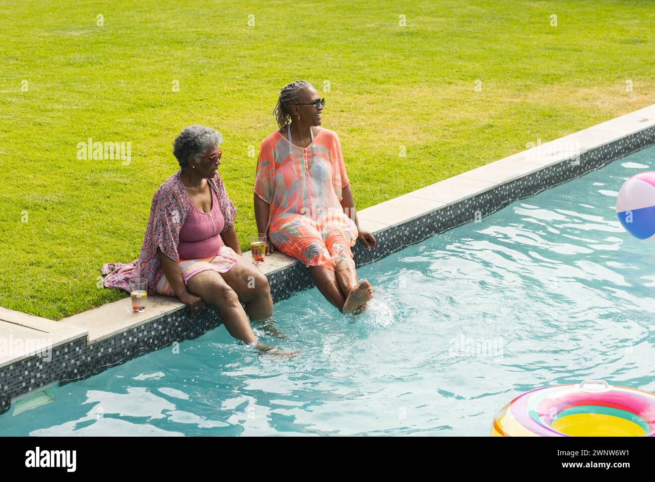 Due donne si godono una giornata di sole in piscina e le gambe sono immerse nell'acqua. Foto Stock