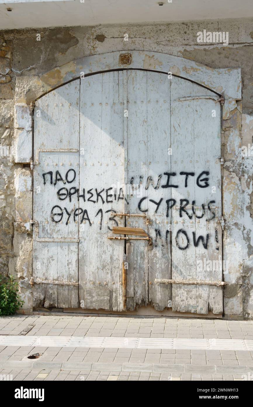 Graffiti politici su una vecchia porta di legno di un'officina. Unitevi Cipro ora. Larnaca, Cipro. Febbraio 2024 Foto Stock