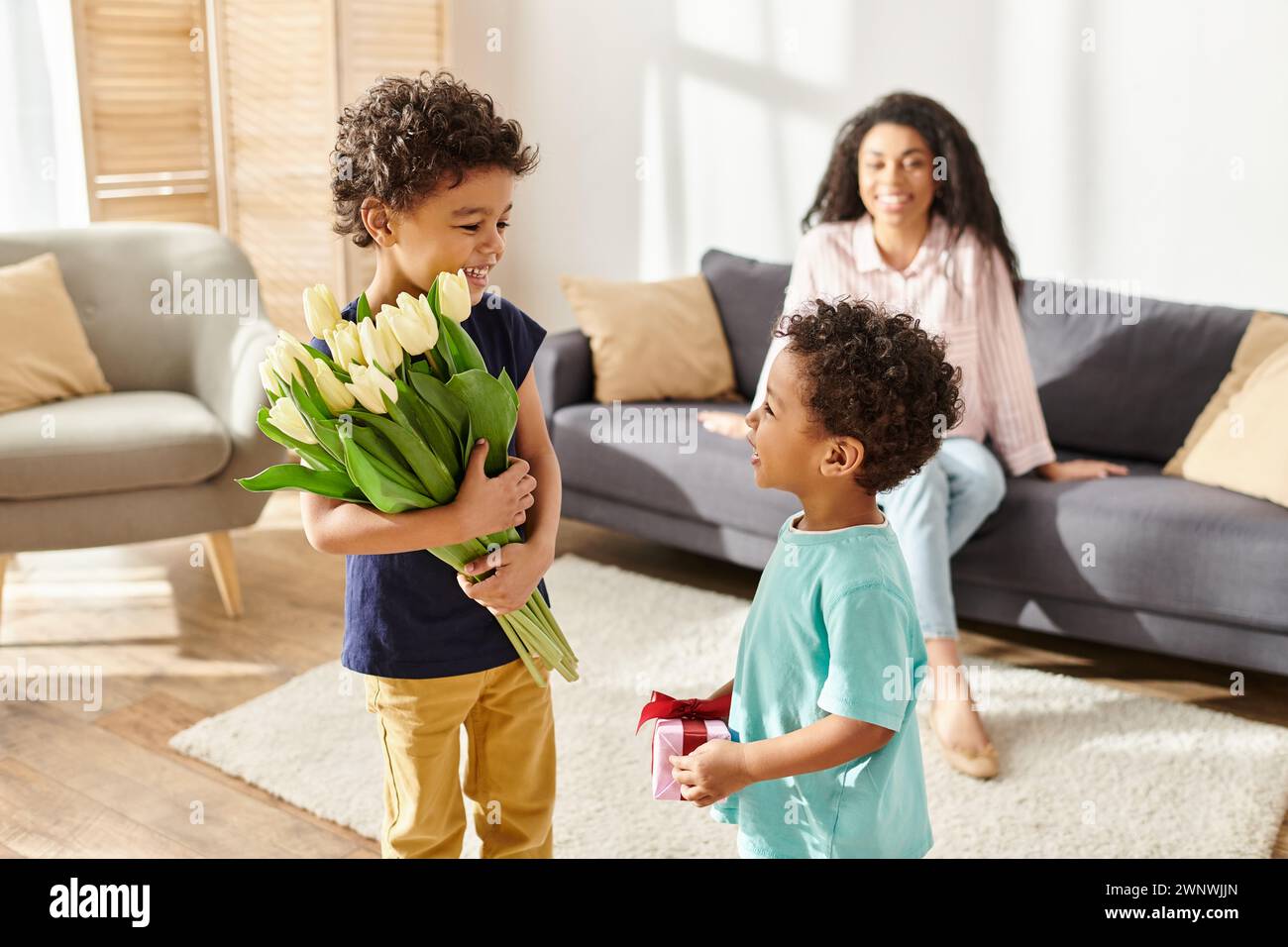 Concentrati sui ragazzi afroamericani che tengono fiori e regali accanto alla loro mamma sfocata, la festa della mamma Foto Stock