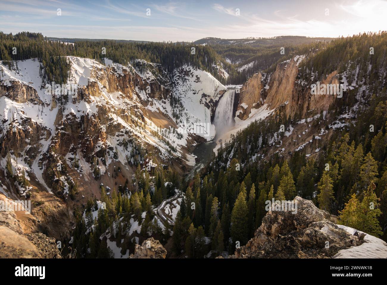 Un'incantevole immagine di una potente cascata che si getta attraverso un paesaggio innevato, tagliando attraverso le aspre scogliere circondate da alberi di pino Foto Stock