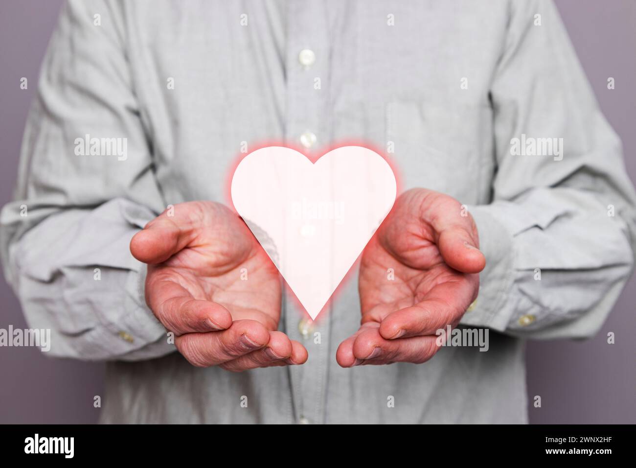 Primo piano delle mani di una persona irriconoscibile con una forma di cuore fluttuante. Foto Stock