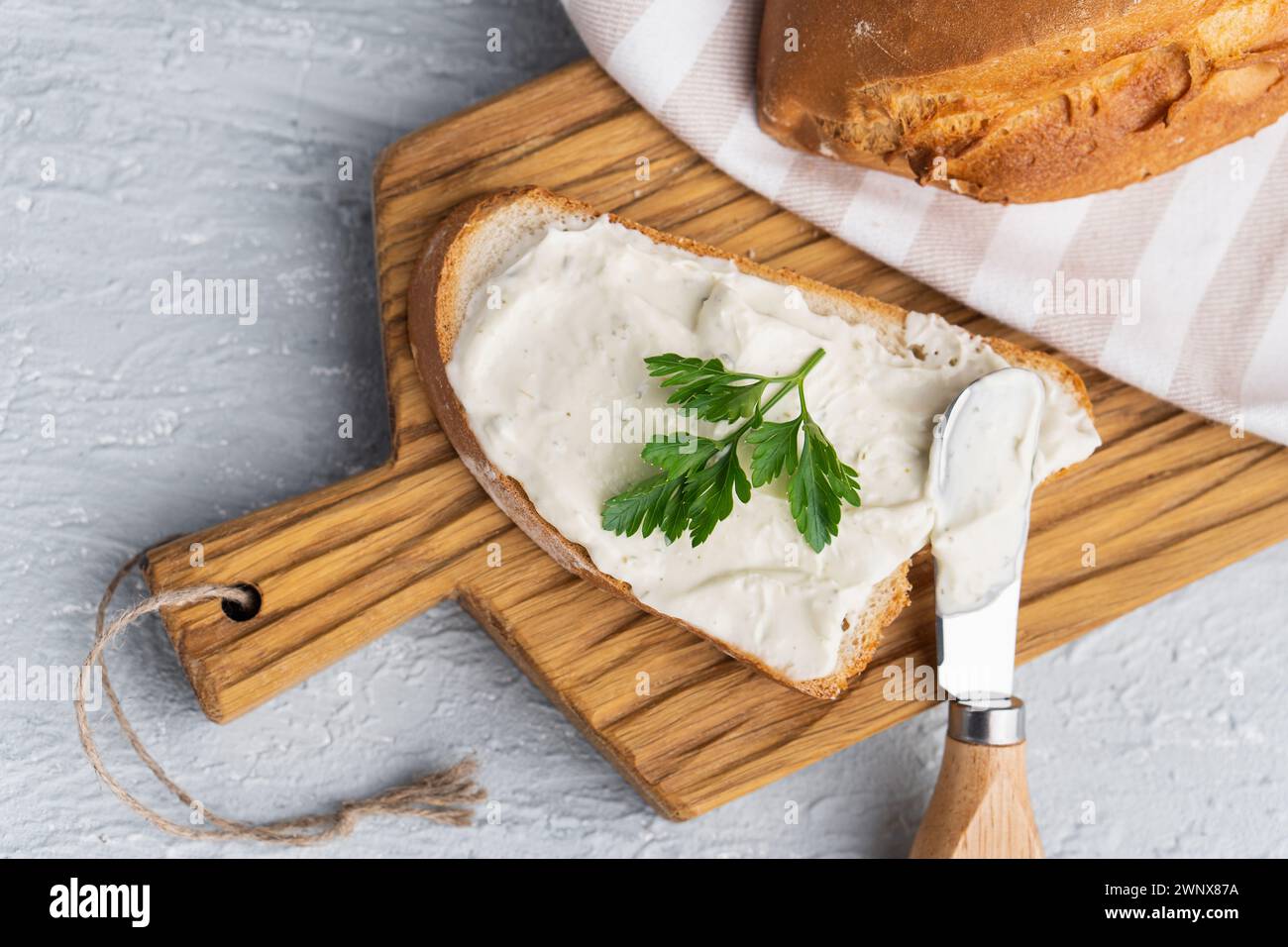 Formaggio cremoso con erbe aromatiche e condimento su fetta di pane fresco di segale croccante con coltello per formaggio nelle vicinanze Foto Stock