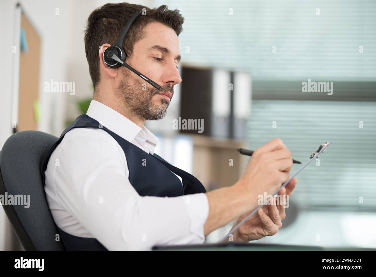 uomo in ufficio che indossa la cuffia e scrive sugli appunti Foto Stock