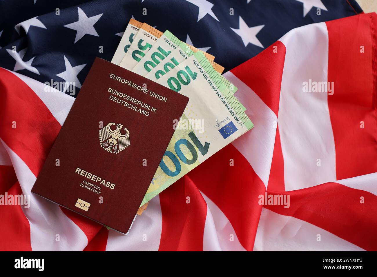 Passaporto tedesco rosso dell'Unione europea e denaro sullo sfondo della bandiera nazionale degli Stati Uniti da vicino. Concetto di turismo e diplomazia Foto Stock