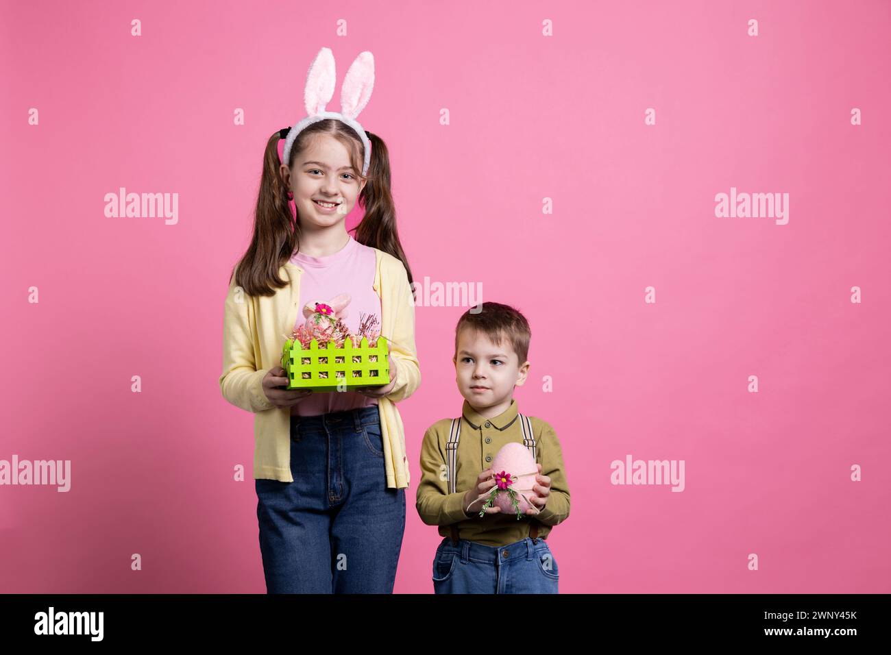 Bambini piccoli e carini che mostrano gli ornamenti e i giocattoli pasquali in studio, in posa per un servizio fotografico per le festività natalizie. Fratellino e sorella si sentono entusiasti della festa primaverile e dei regali. Foto Stock