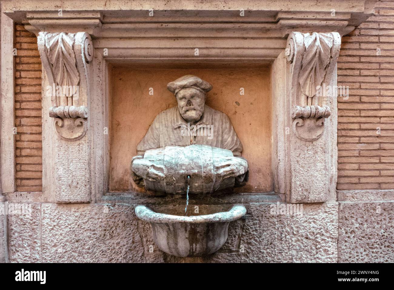 Statua di un uomo che tiene una botte che forma una fontana pubblica sulle mura esterne di un edificio storico nel centro di Roma. Foto Stock