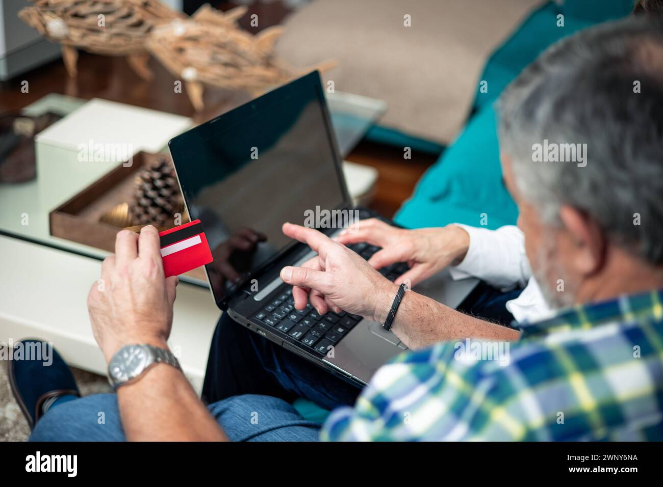 primo piano da dietro coppia in pensione con carta di credito rossa in mano che punta sullo schermo del computer seduto sul divano Foto Stock