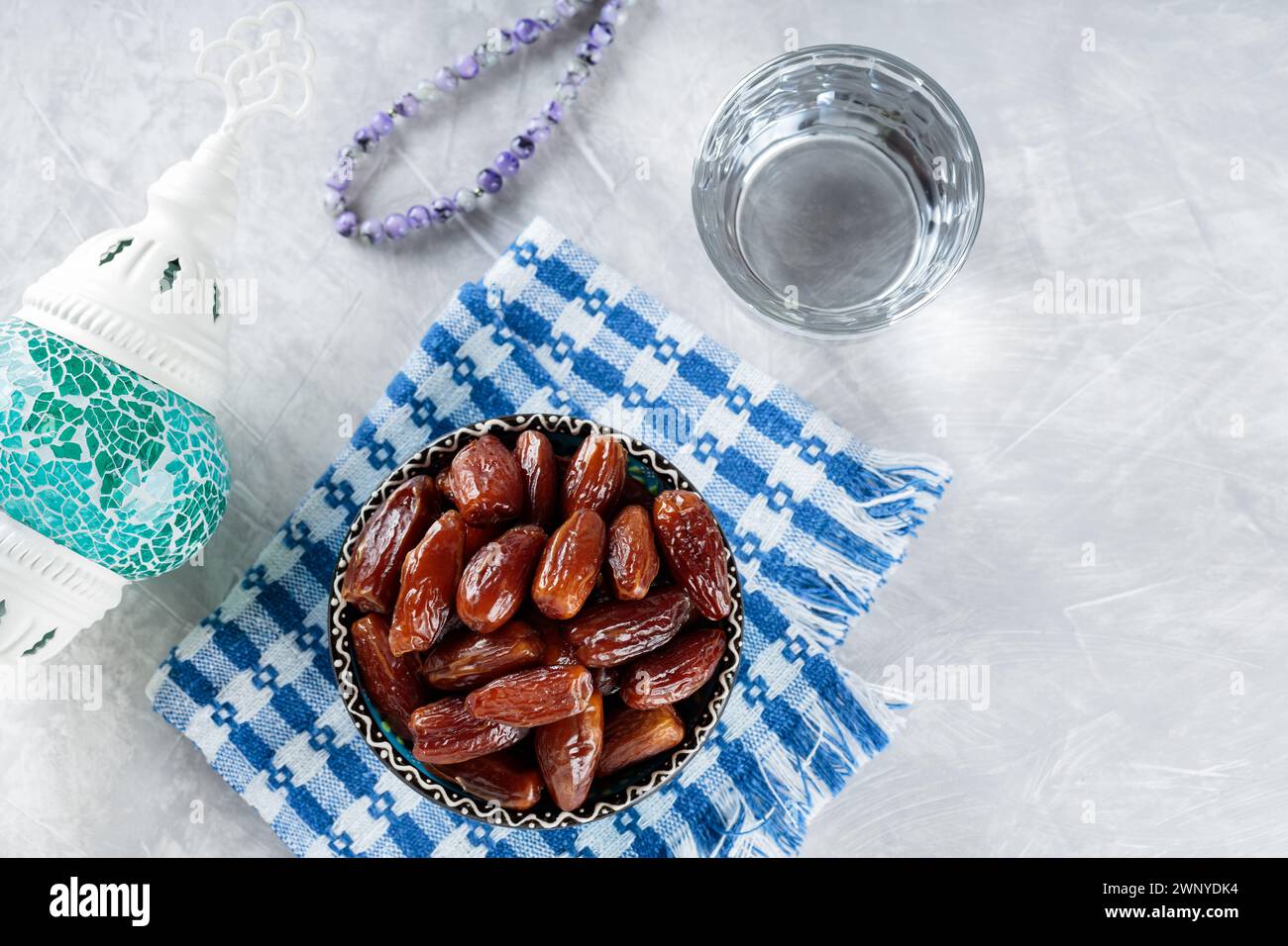 Datteri secchi ciotola su tovagliolo, bicchiere d'acqua e perline di preghiera su sfondo grigio, concetto Ramadan Suhoor, spazio copie Foto Stock