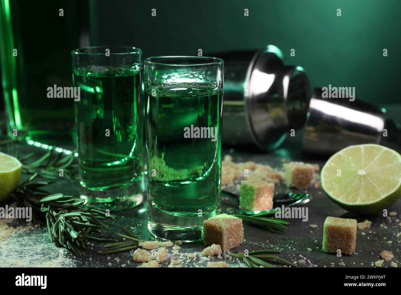 Absinthe in bicchieri da shot, cucchiaio, zucchero di canna, lime e rosmarino su un tavolo grigio, primo piano. Bevanda alcolica Foto Stock