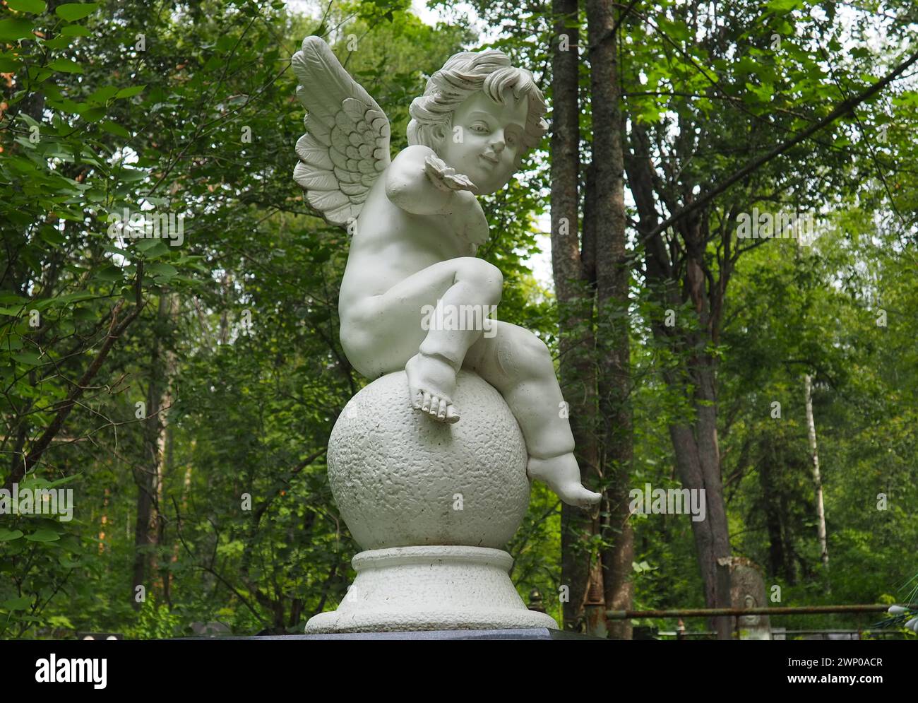 Angelo nel cimitero. Monumento alla tomba di un bambino. Scultura a forma di angelo in marmo o gesso sullo sfondo di alberi Foto Stock