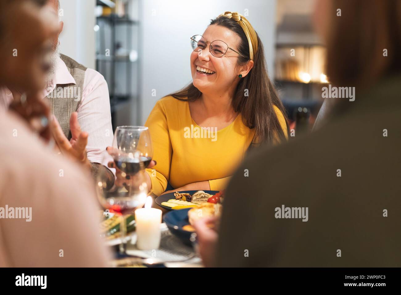 Donna di colore giallo che ride gioiosamente con gli amici durante una cena informale - caldo ritrovo sociale con cibo e bevande Foto Stock