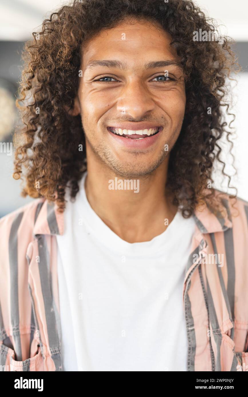 Giovane uomo birazziale con i capelli castani ricci sorride calorosamente Foto Stock