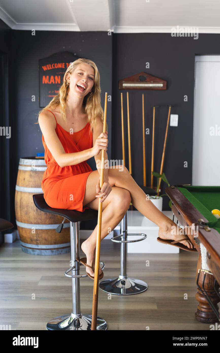 La giovane donna caucasica con un vestito arancione gioca a biliardo in una sala giochi Foto Stock