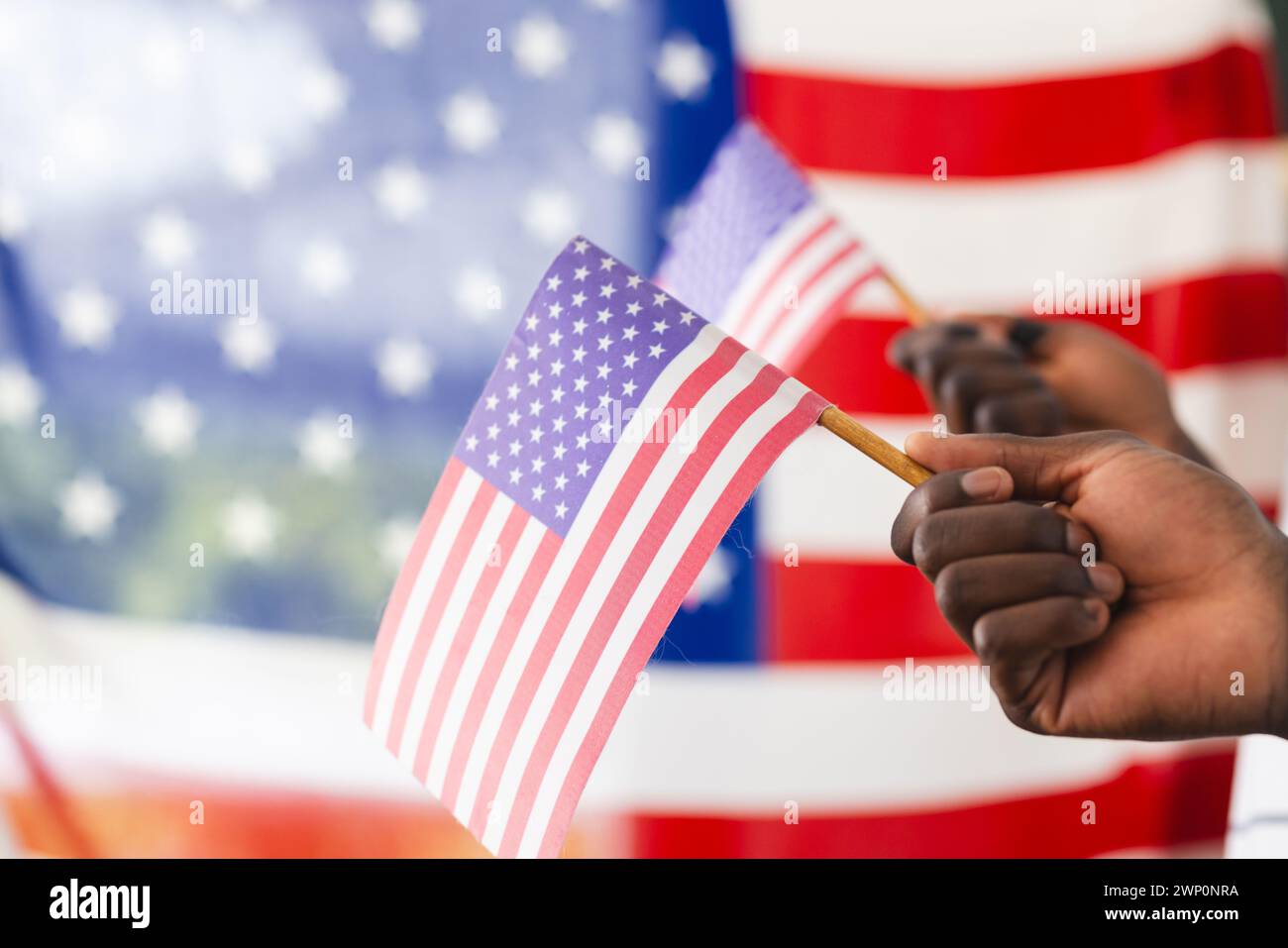 Mano afroamericana con una piccola bandiera americana, con una bandiera più grande sullo sfondo Foto Stock