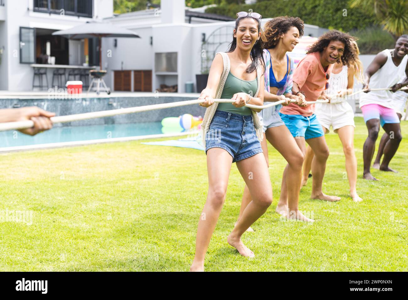 Gruppi diversi di amici si divertono con un tiro alla fune su un prato soleggiato con spazio per copiare Foto Stock
