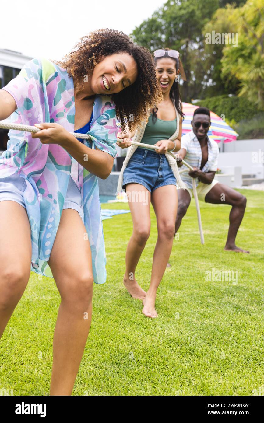 Le giovani donne birazziali e un afroamericano si divertono in una partita di tiro alla fune all'aperto Foto Stock