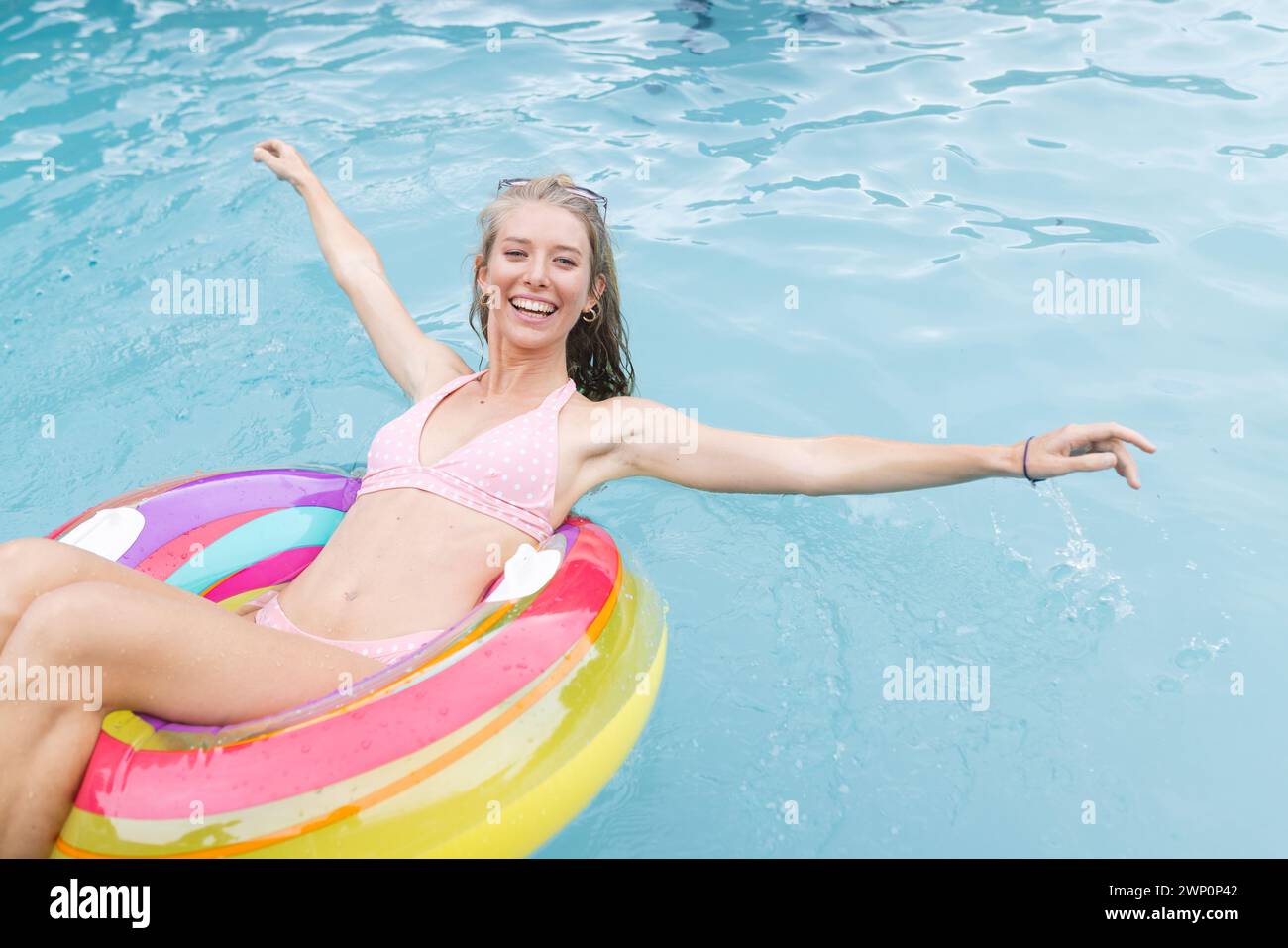 La giovane donna caucasica gode della piscina, rilassandosi su un galleggiante colorato in un bikini rosa Foto Stock
