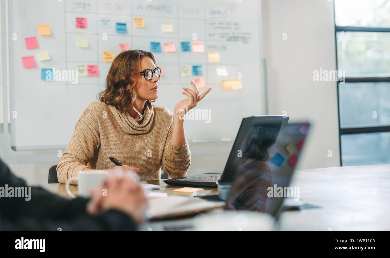 Donna impegnata in una sessione di brainstorming collaborativa con i colleghi in una sala riunioni. Gli uomini d'affari discutono idee e gestiscono progetti. Lo faranno Foto Stock