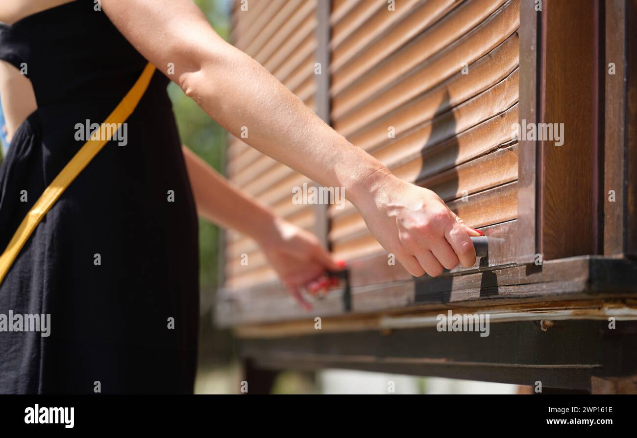 Le mani femminili tengono le maniglie del fermo di legno aprono le tende di legno all'aperto closeup Foto Stock