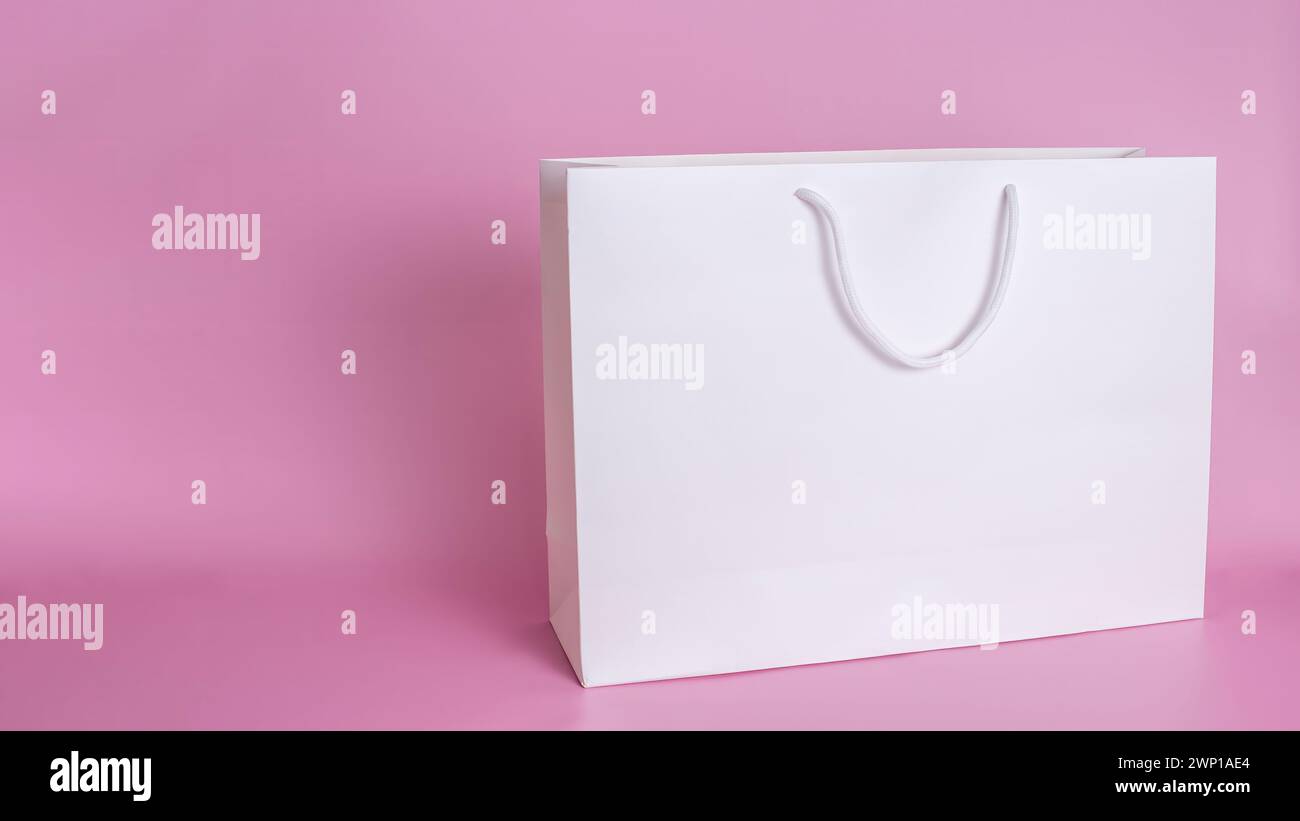 Un grande sacchetto di carta bianca pulito con manici di corda bianchi si staglia su uno sfondo rosa in primo piano. Foto Stock