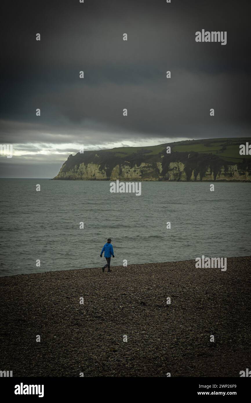 Persona che cammina sulla spiaggia di ciottoli vicino alla città di Seaton, Devon Foto Stock