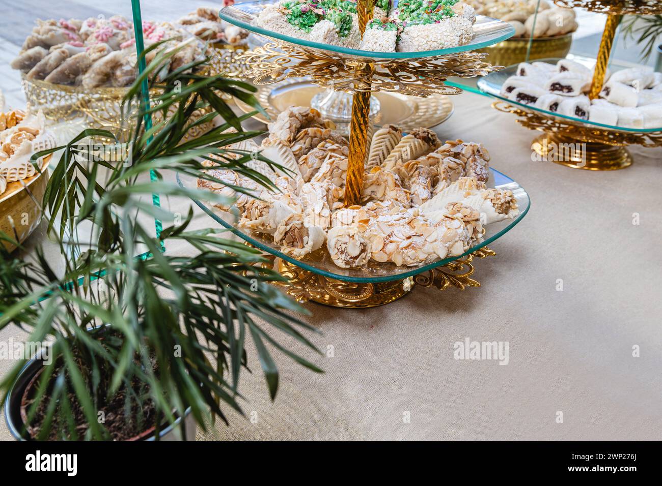 Foto orizzontale una squisita selezione di dolci arabi elegantemente disposti su banchi dorati ornati, completati da verdeggianti fronde di palme. Cibo e cul Foto Stock