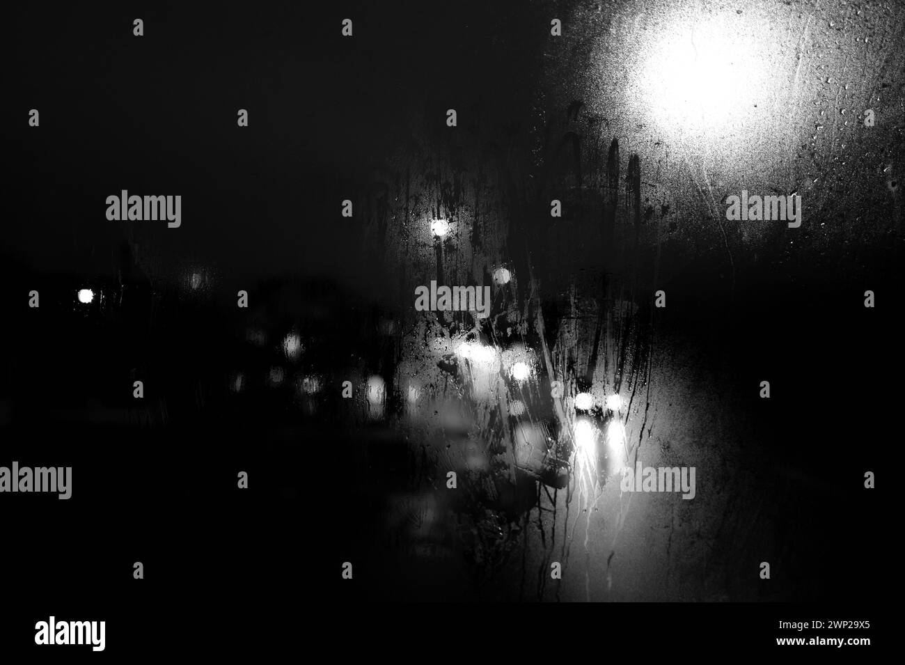 Vista notturna invernale in bianco e nero attraverso la finestra dell'autobus, i semafori, i fari per auto, i semafori, i semafori, finestra nebbiosa e gocce di pioggia Foto Stock