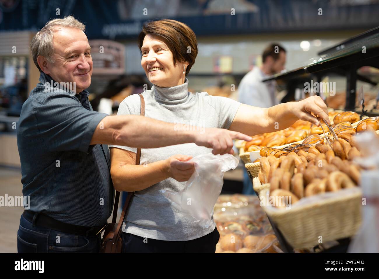 Una coppia di anziani sposati sceglie panini caldi e freschi e pane alla vetrina del supermercato Foto Stock