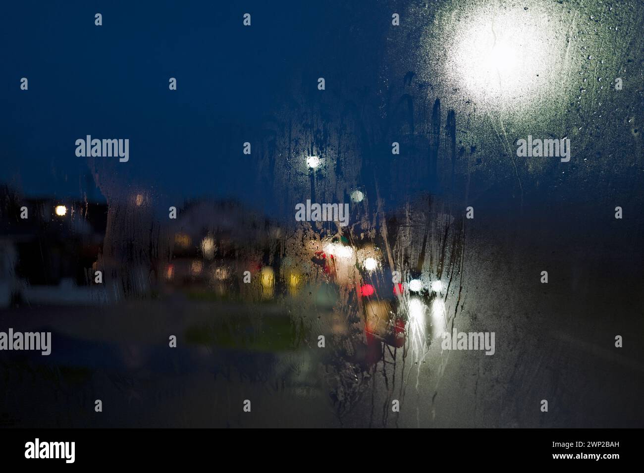 Vista notturna invernale a colori dalla finestra dell'autobus, dai semafori, dai fari per auto, dai semafori, dai semafori, finestra nebbiosa e gocce di pioggia Foto Stock