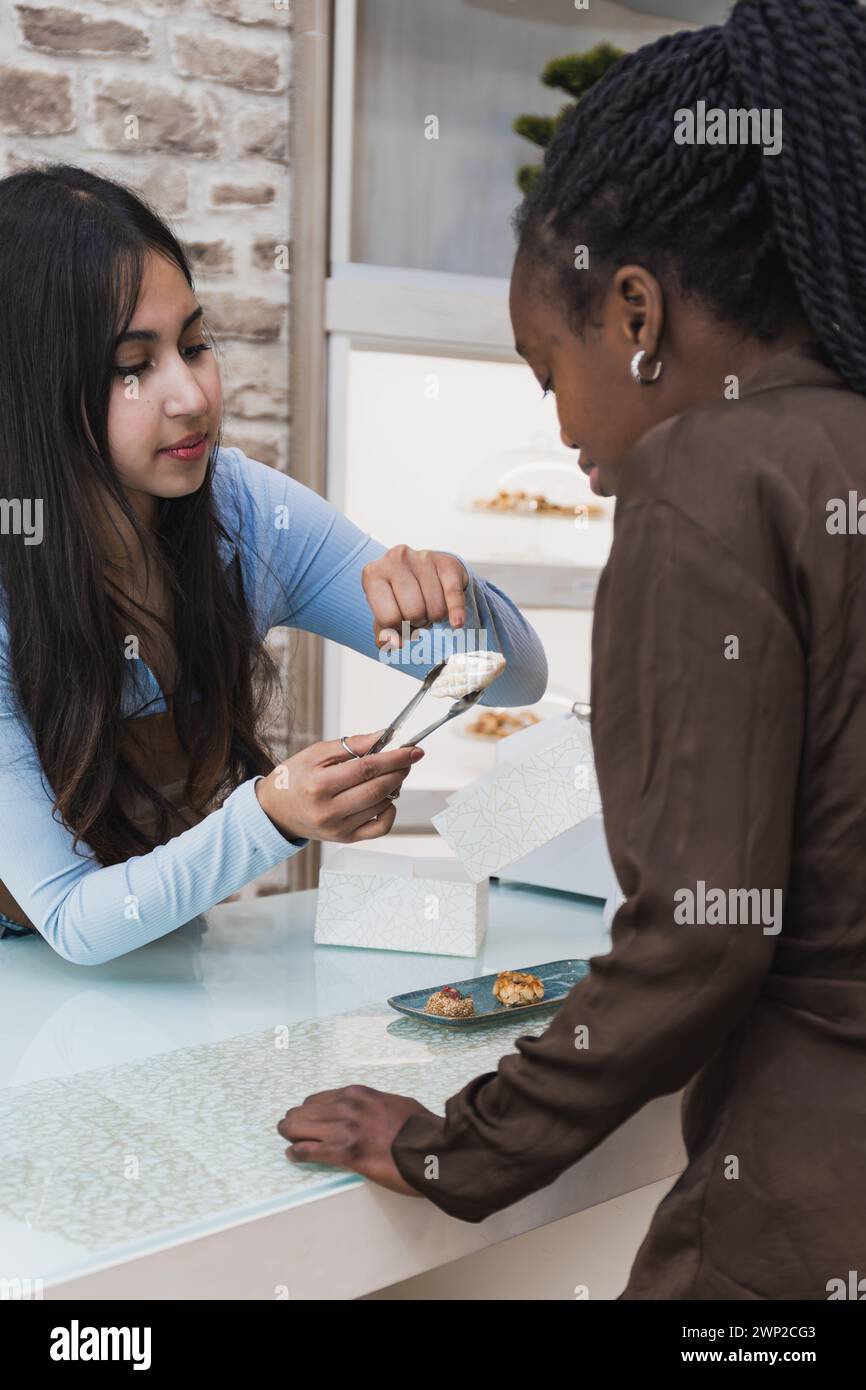 Foto verticale un server dedicato in una pasticceria offre un assaggio di un dolce delicato a un cliente interessato. Cibo e cultura c Foto Stock