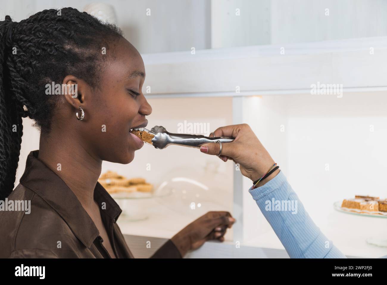 Foto orizzontale un cliente gioioso assaggia un assaggio di pasticceria del Medio Oriente, offerto da un cameriere da una mostra di dessert speciali. Cibo e. Foto Stock
